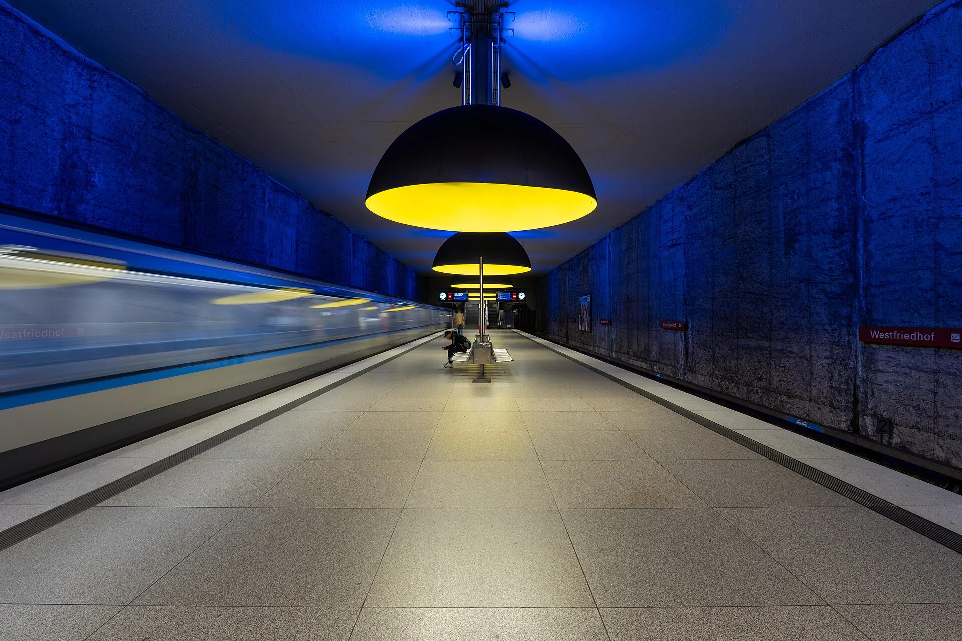 Underground platform with large dome lamps casting warm light and rough walls washed in blue